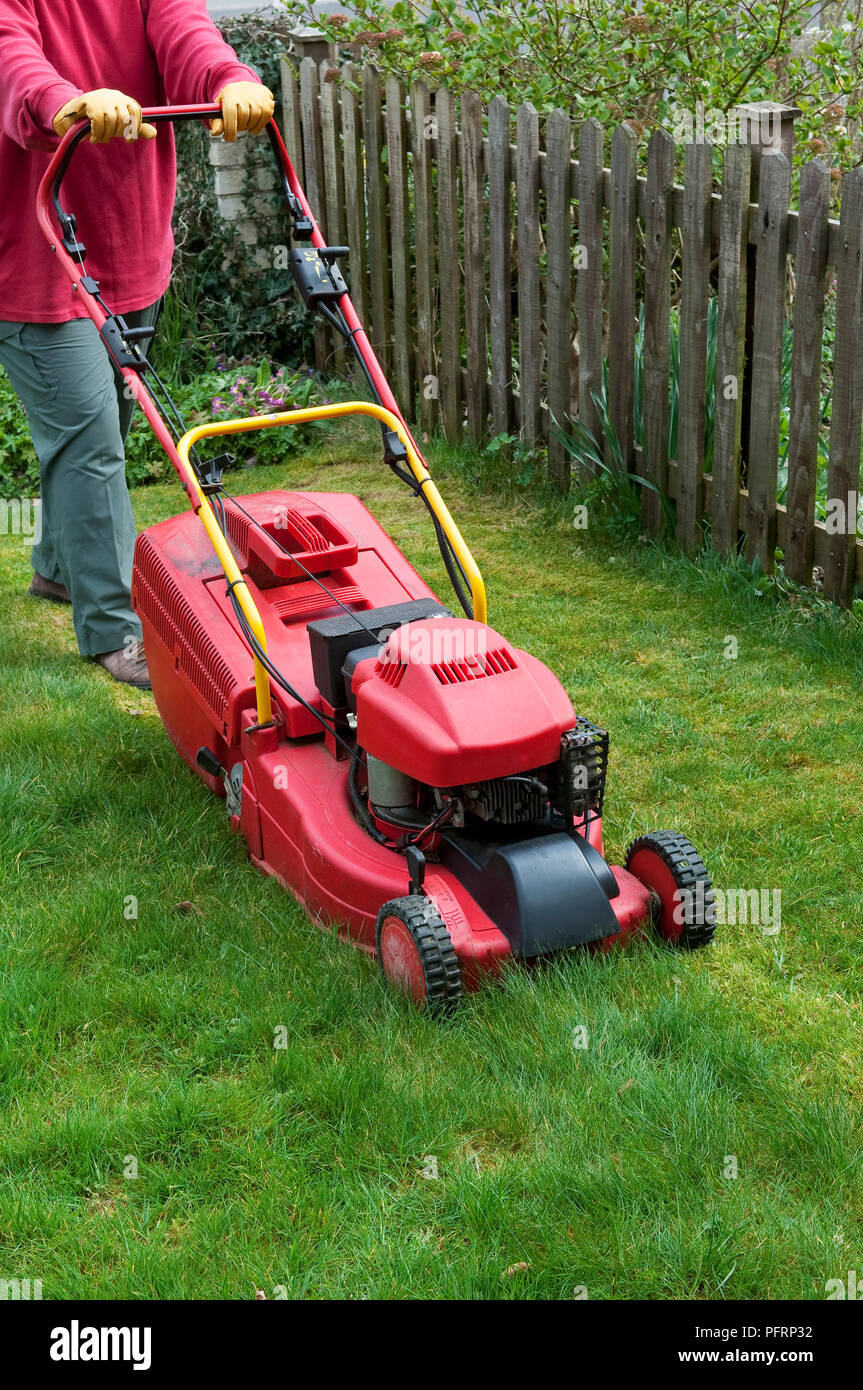 Person mowing long grass on lawn using rotary mower Stock Photo Alamy