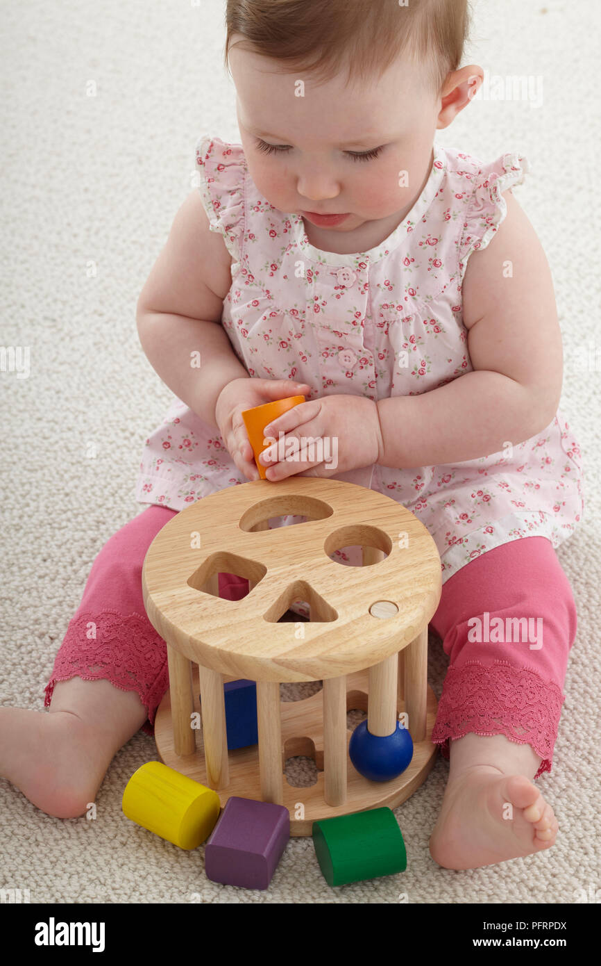 Baby girl (8.5 months) playing with wooden blocks, to be inserted in