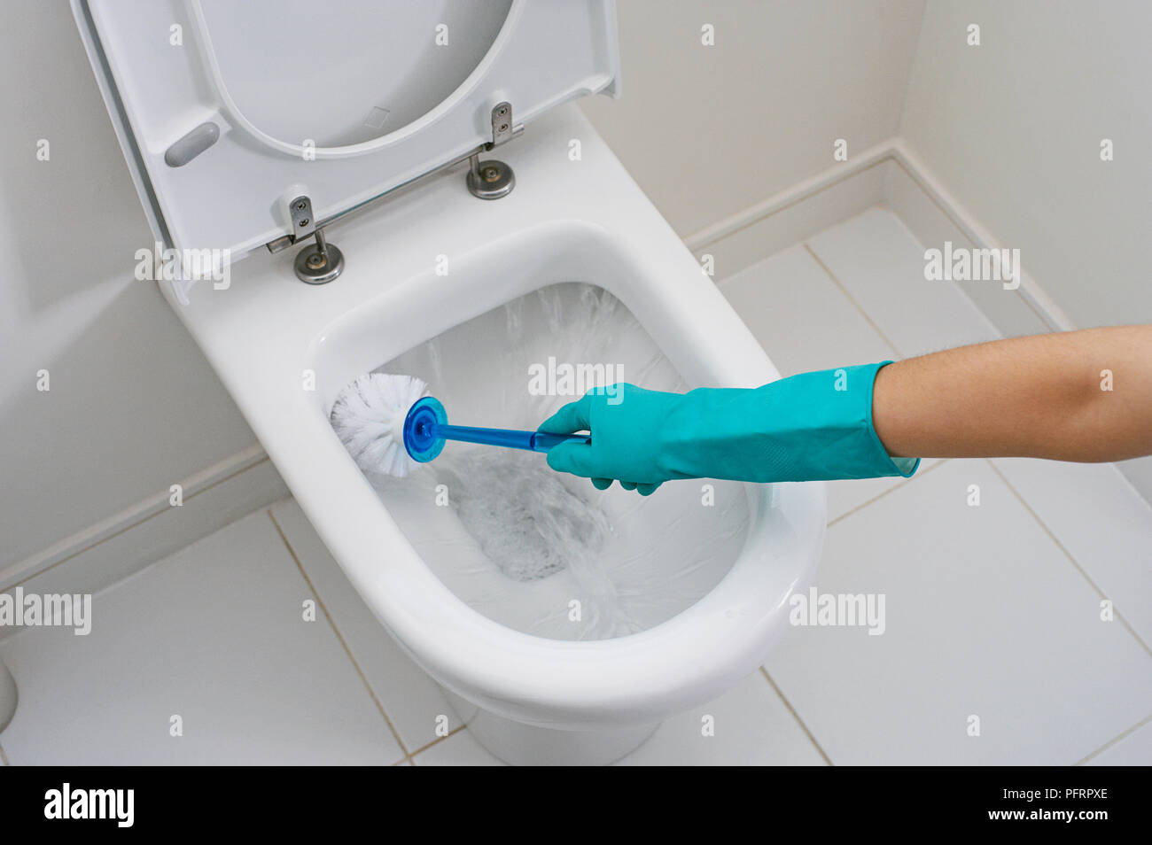 Woman wearing washing up gloves to clean toilet with brush and flushing water Stock Photo