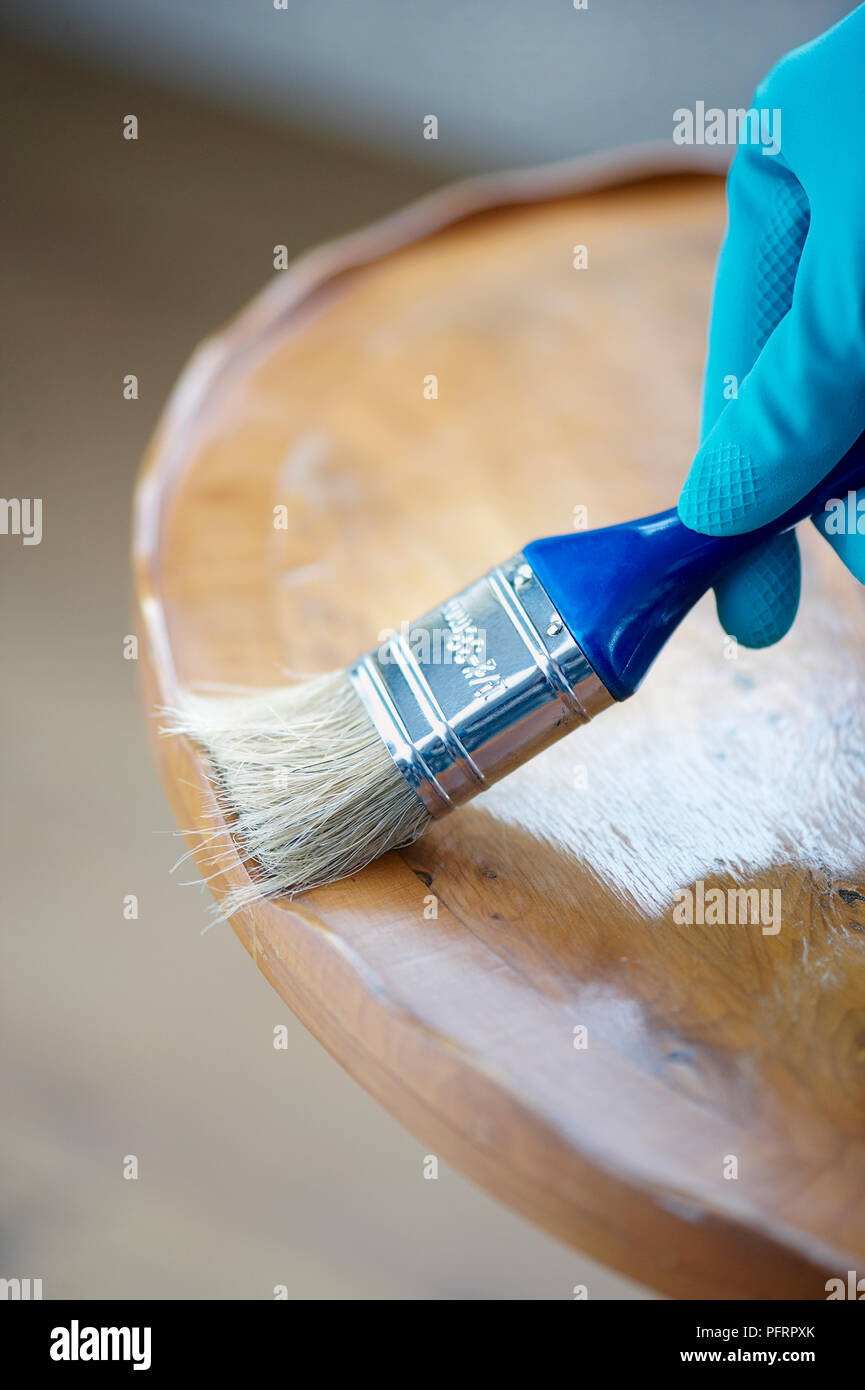 Using paintbrush to remove dust from edge of round wooden table Stock