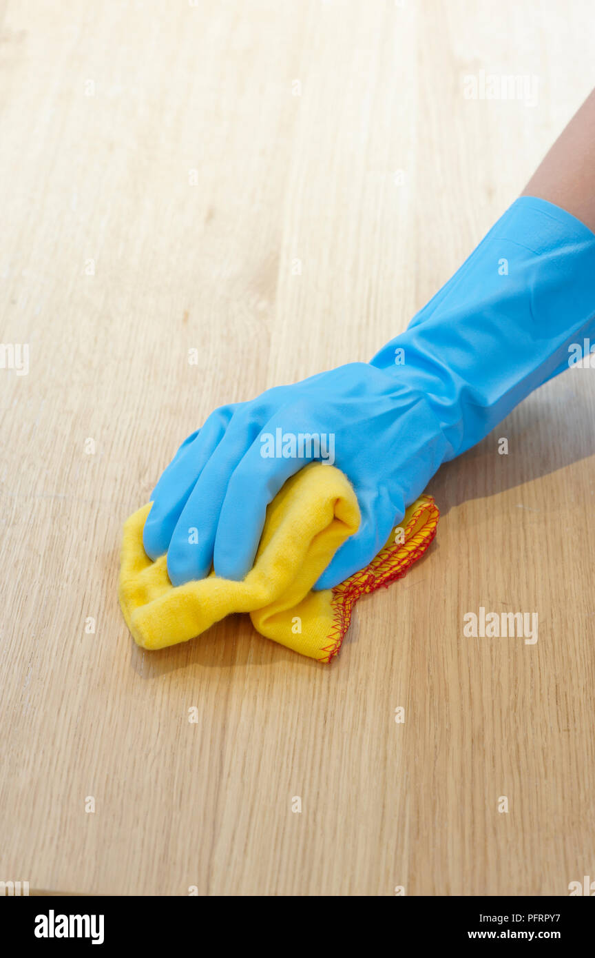 Hand wearing blue washing up glove to polish wooden table using yellow ...