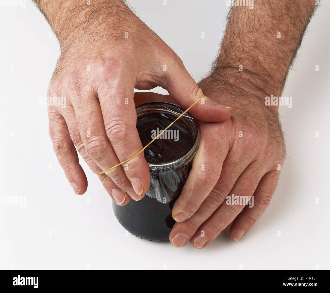 Jar of jelly being sealed with cellophane and elastic band Stock Photo