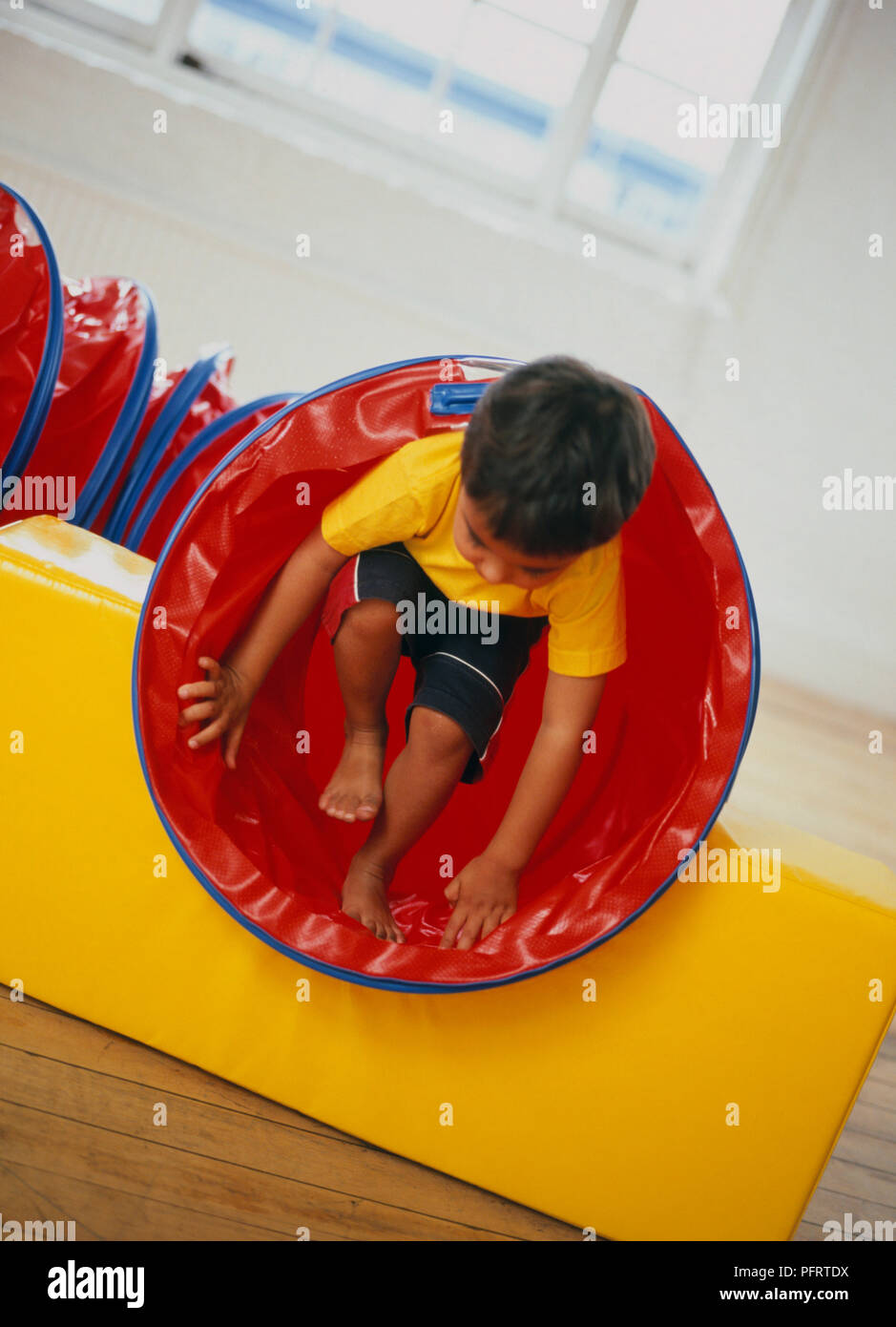 Barefoot toddler wearing yellow Tshirt and black shorts climbing out