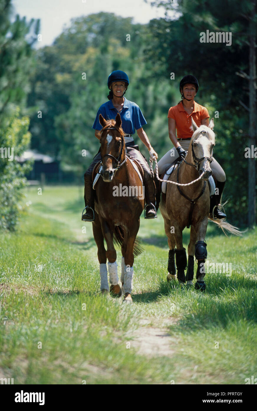 Two women riding through countryside, one leading horse by lead rein