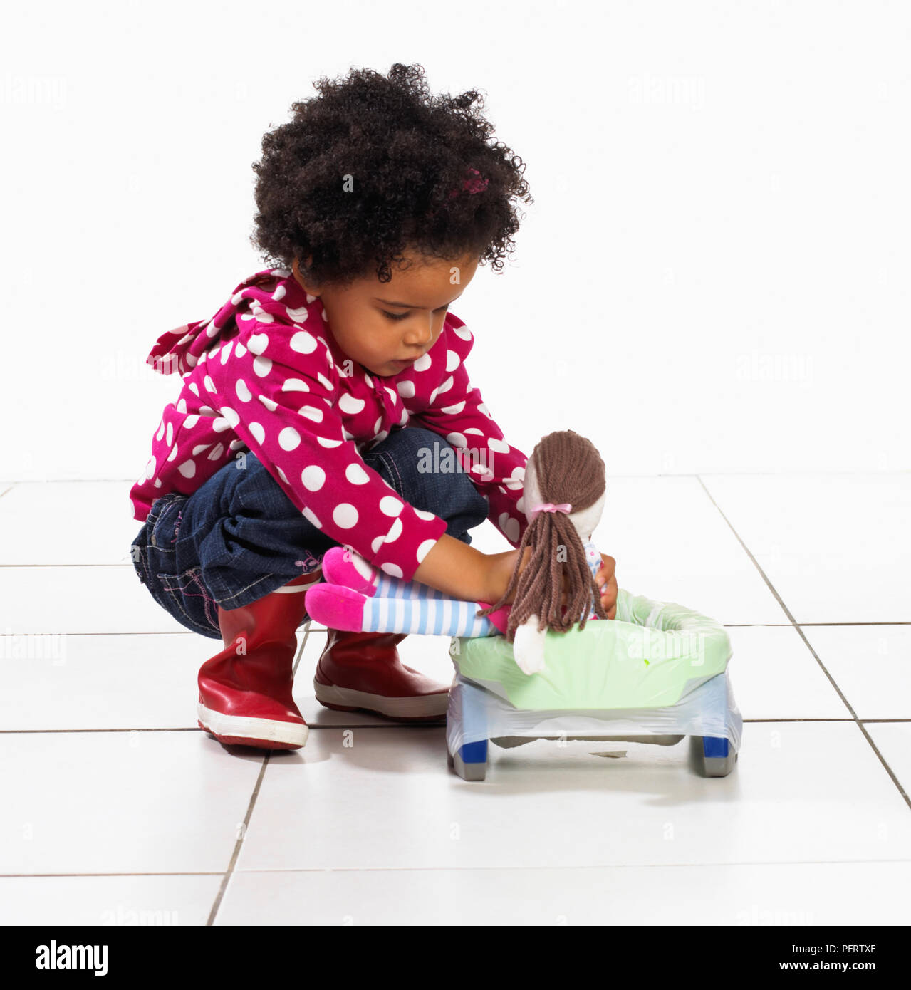 Toddler girl sitting doll on portable potty, 2 years Stock Photo