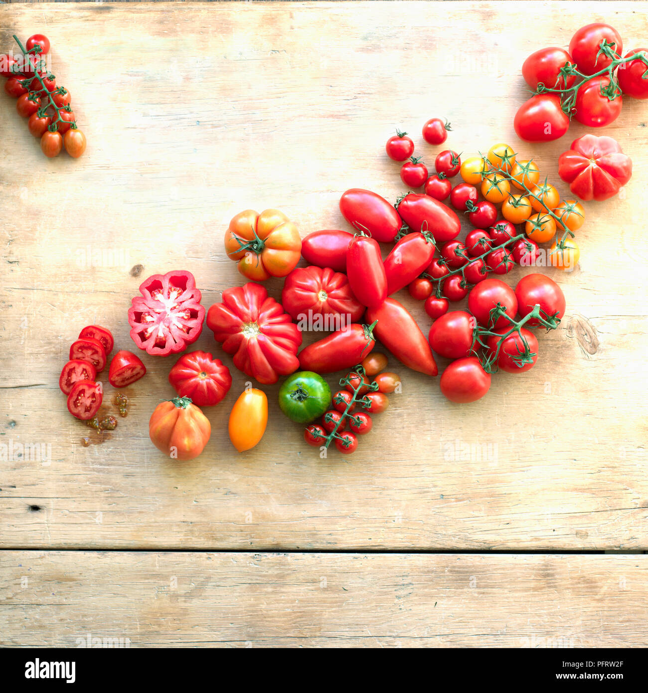 A selection of tomatoes of different shapes, sizes, and colours on wood background Stock Photo