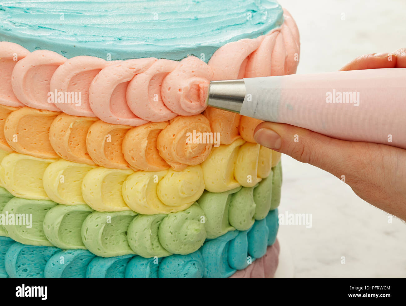 Piping coloured icing on cake, rainbow cake Stock Photo