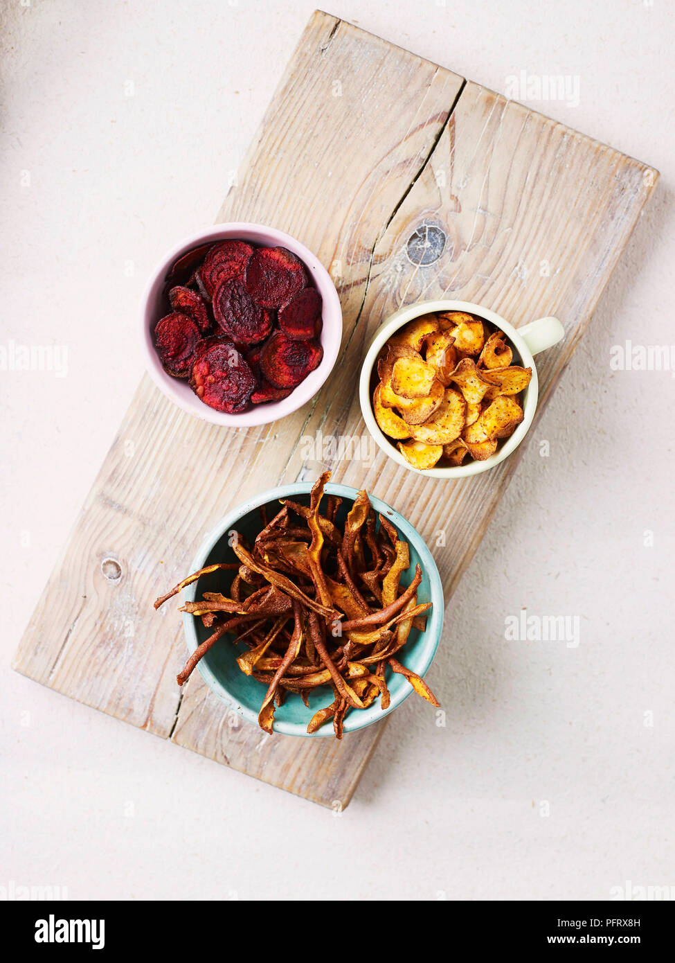 Vegetable crisps (parsnip, beetroot, sweet potato) in bowls on a wooden board Stock Photo