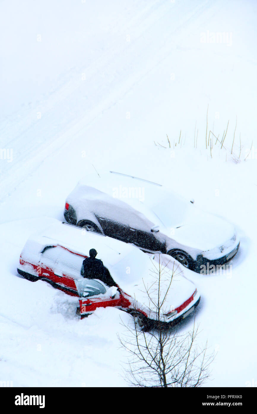 Male driver trying to free his car from snowy captivity. Parked cars covered with snow. Bad weather in town. Snowy day. Urban scene. Weather concept.  Stock Photo