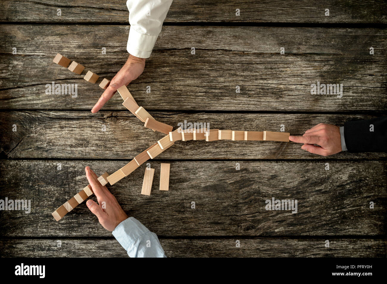 Top view of male hand pushing dominos placed in Y shape knocking them down and two other hands stopping them each on one side. Conceptual of crisis ma Stock Photo