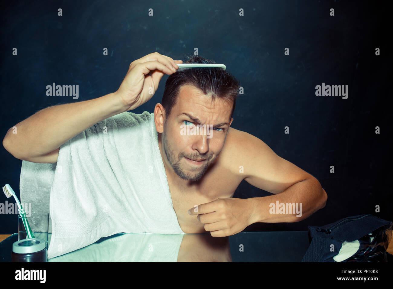 Man With Comb Concerned About Hair Loss. Close up photo of young caucasian man looking on his face. at home. Human emotions concept. Lifestyle and ski Stock Photo