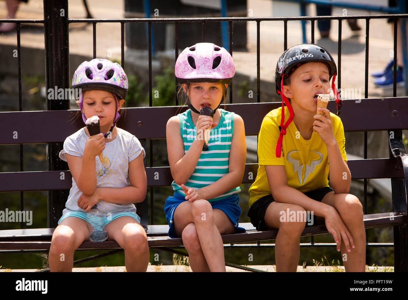 UK, Cornwall, Padstow, The Strand, young chidren wearing bicycle helmets eating ice creams in sunshine Stock Photo