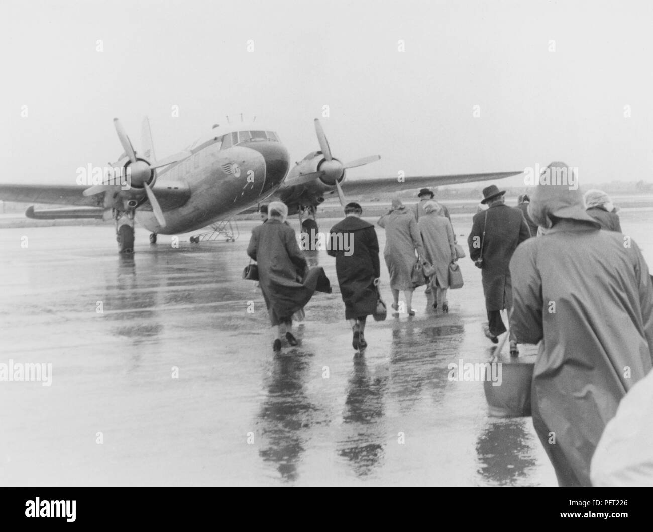 1950s vacation. A group of people are walking in the pouring rain towards the waiting plane bound for Spain. Sweden 1951. ref 385 Stock Photo