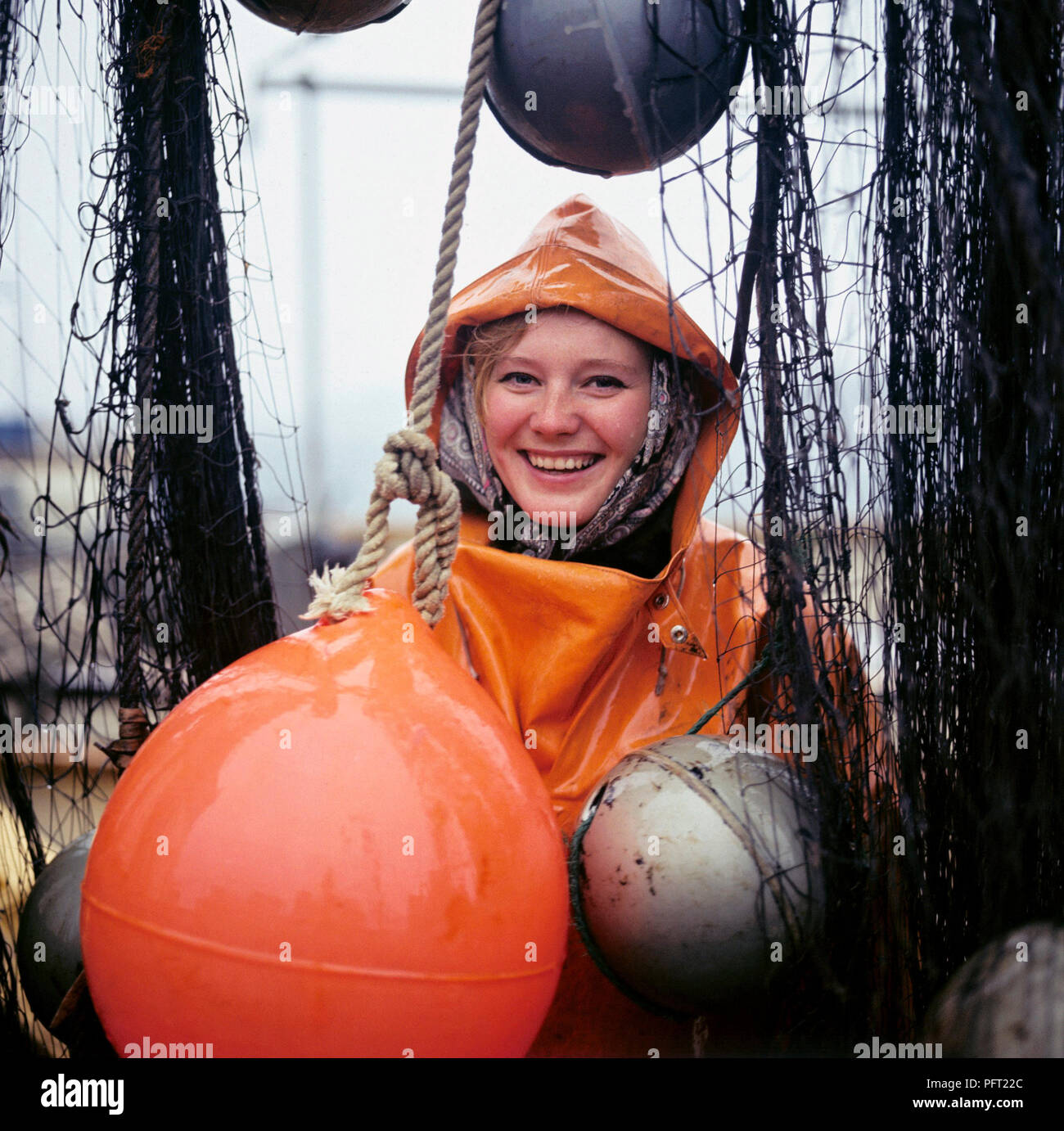 Rain in the 1960s. A young smiling woman is dressed in rain clothes and  poses on a the deck of a fishing vessel with fishing nets. Sweden 1969  Stock Photo - Alamy