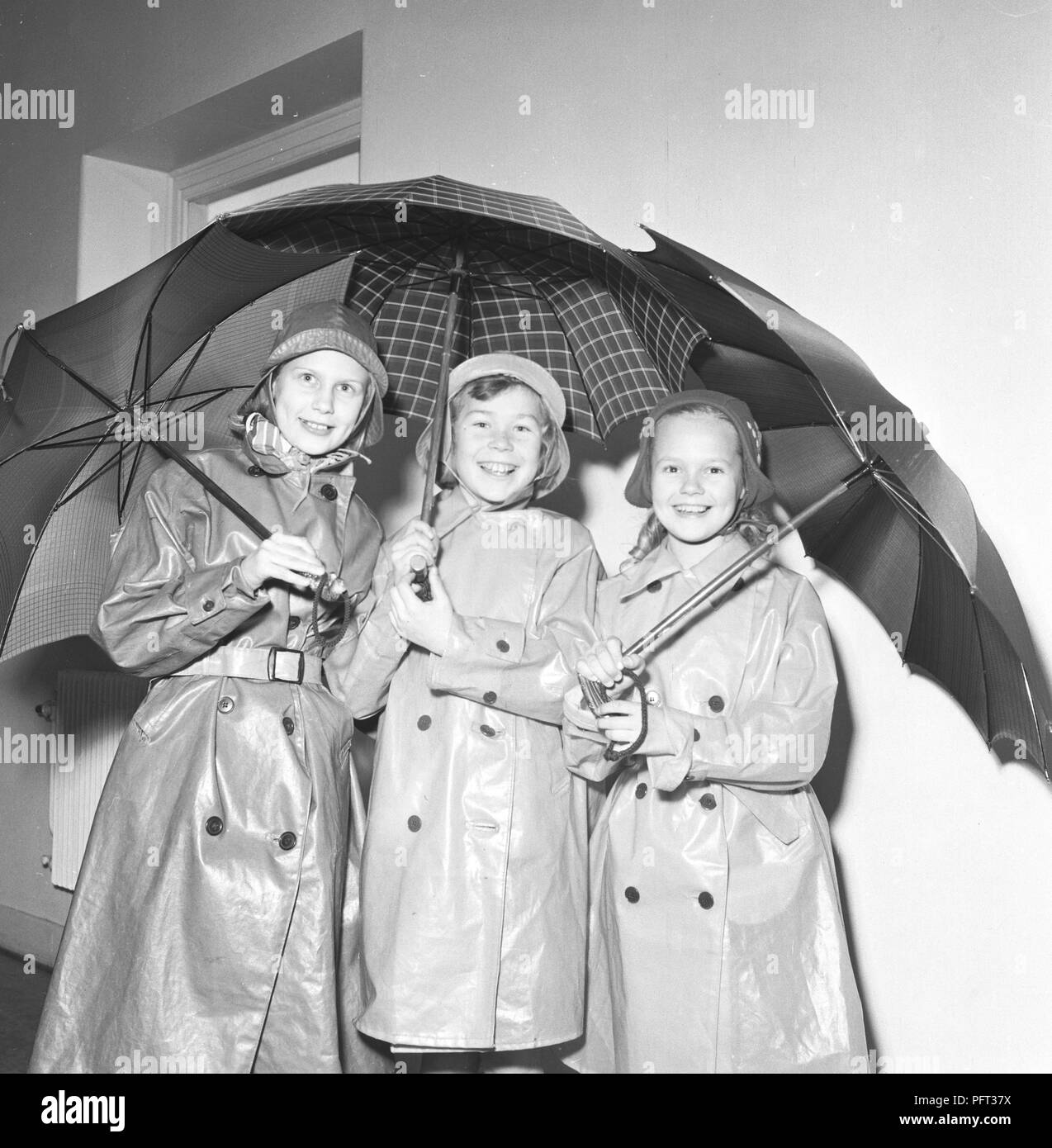 1950s children in rain clothes. Three children are standing togetherdressed in rain coats and rubber holding umbrellas. Sweden November 1952 Stock Photo