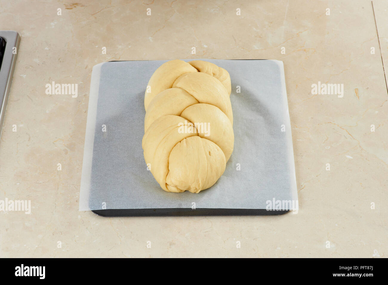 Raw braided Hefekranz loaf on baking tray covered with wax paper on kitchen worktop Stock Photo