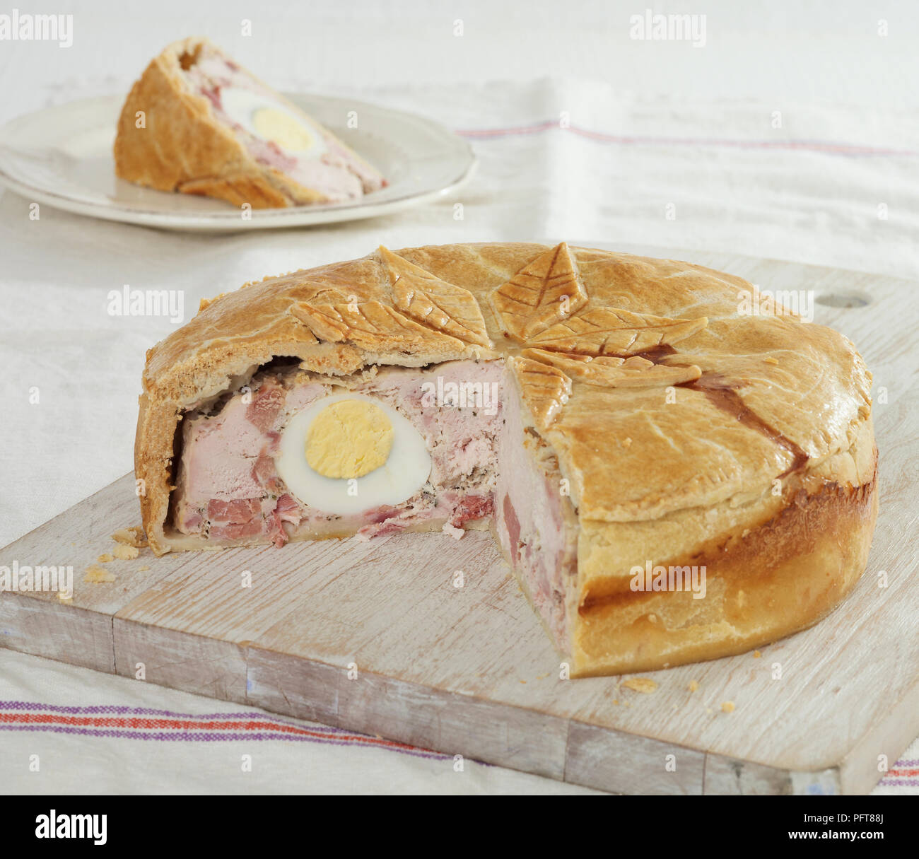 Chicken and ham pie with hardboiled egg on chopping board and plate