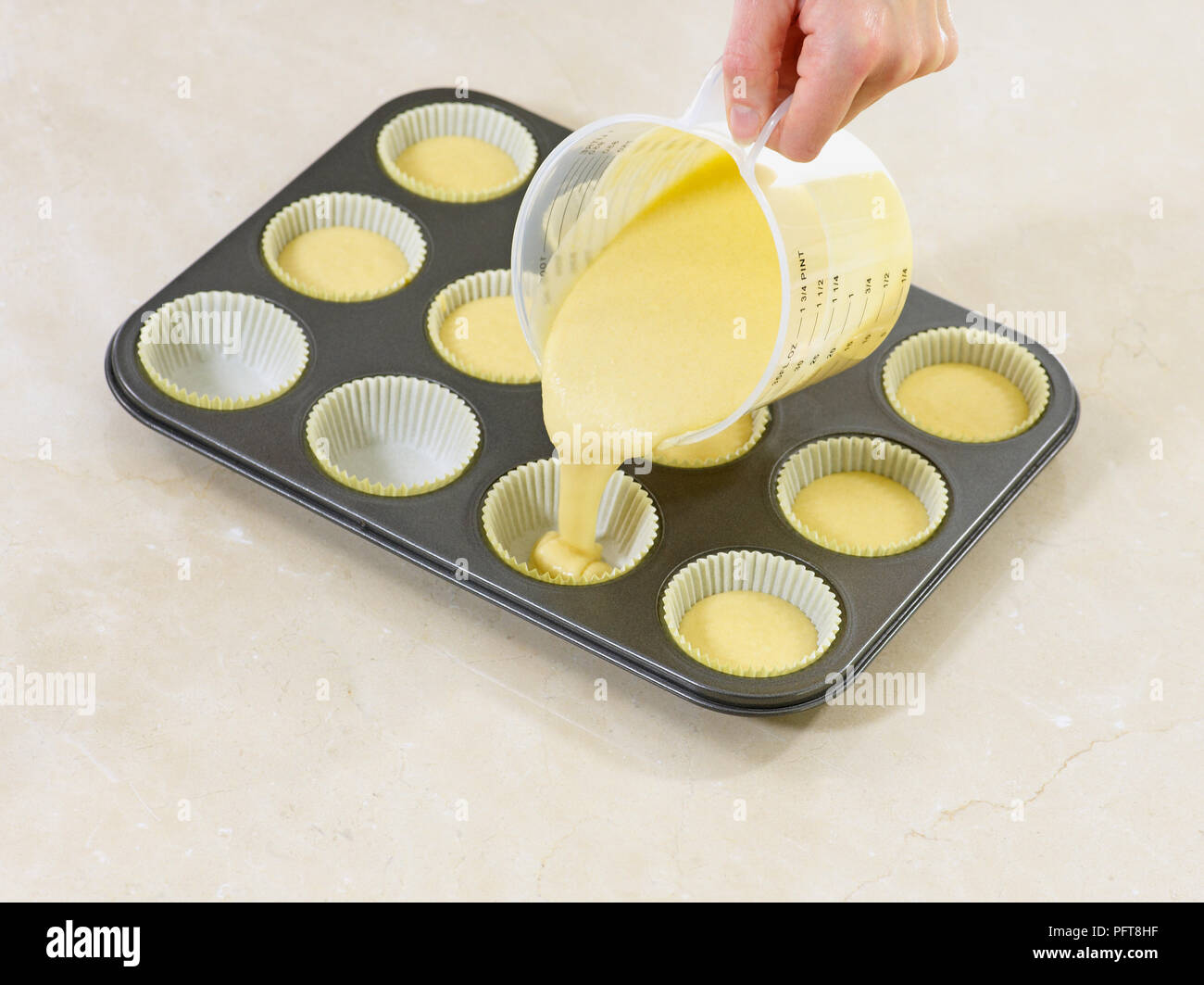 pouring-raw-vanilla-cupcake-mixture-from-measuring-jug-into-cake-cases
