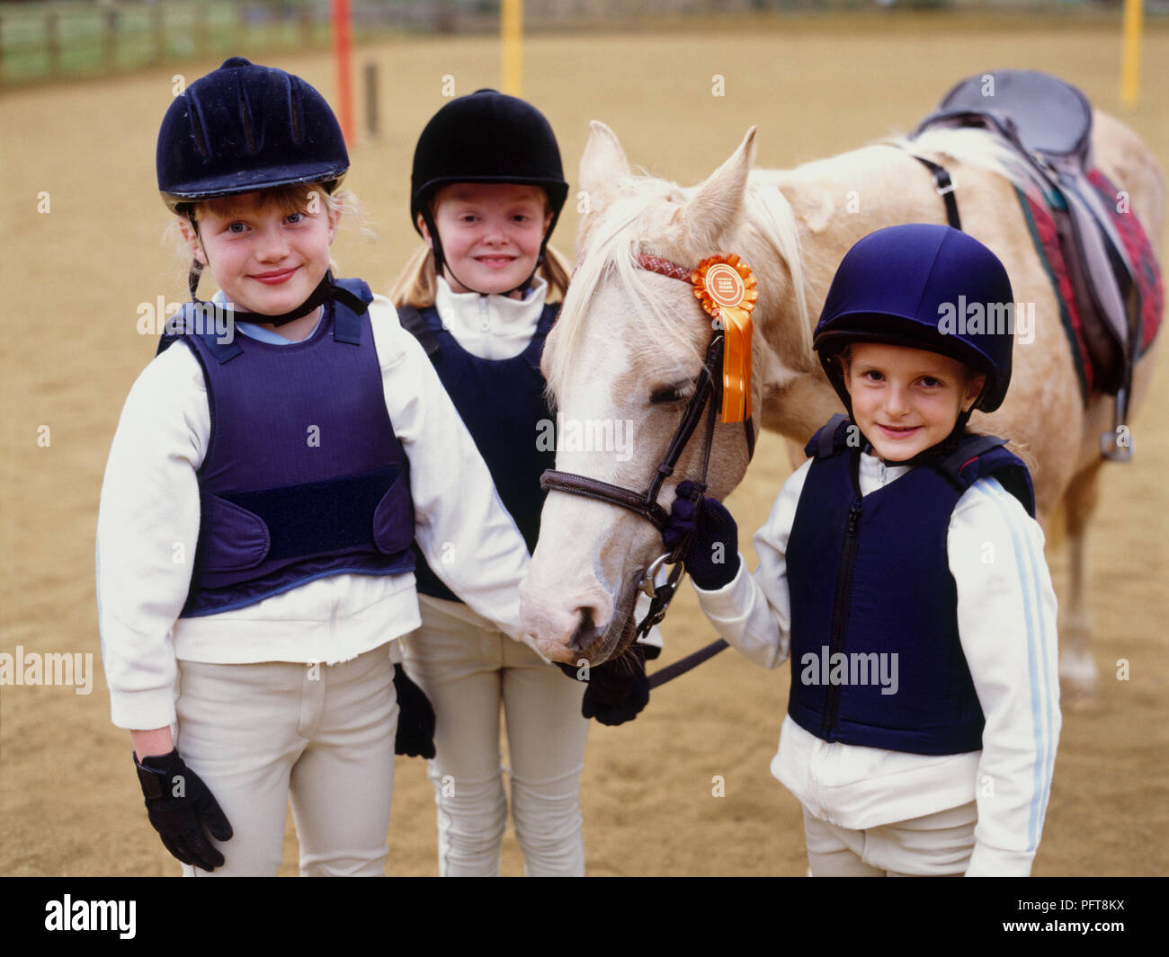 Three young girls in paddock and palomino pony with rosette on bridle Stock Photo