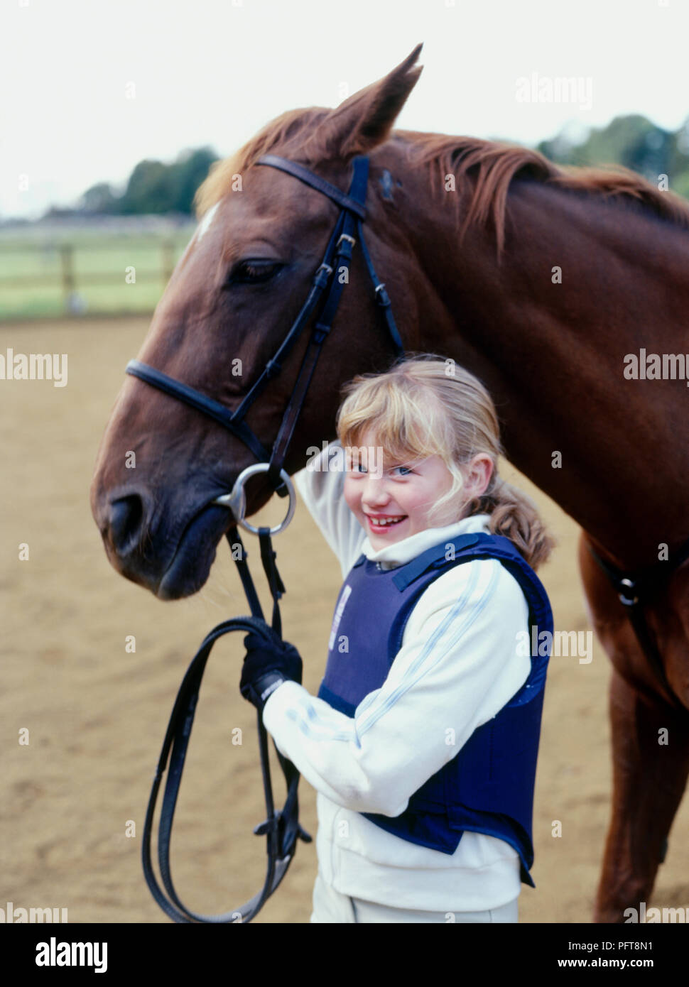 Young smiling girl holding head of chestnut pony and reins in paddock Stock Photo