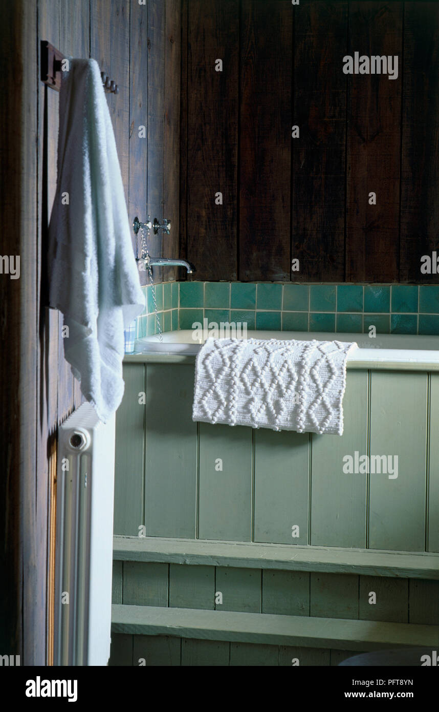 Rustic bathroom with mat on side of bath and towel hanging from hook