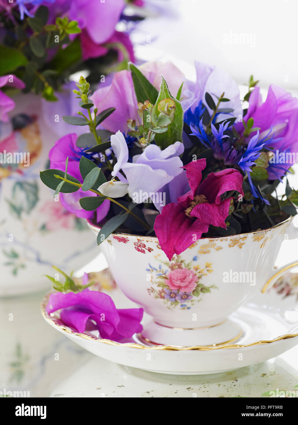 Flowers arranged in floral vintage tea set, clematis, sweet pea, centaurea, eucalyptus parvifolia Stock Photo
