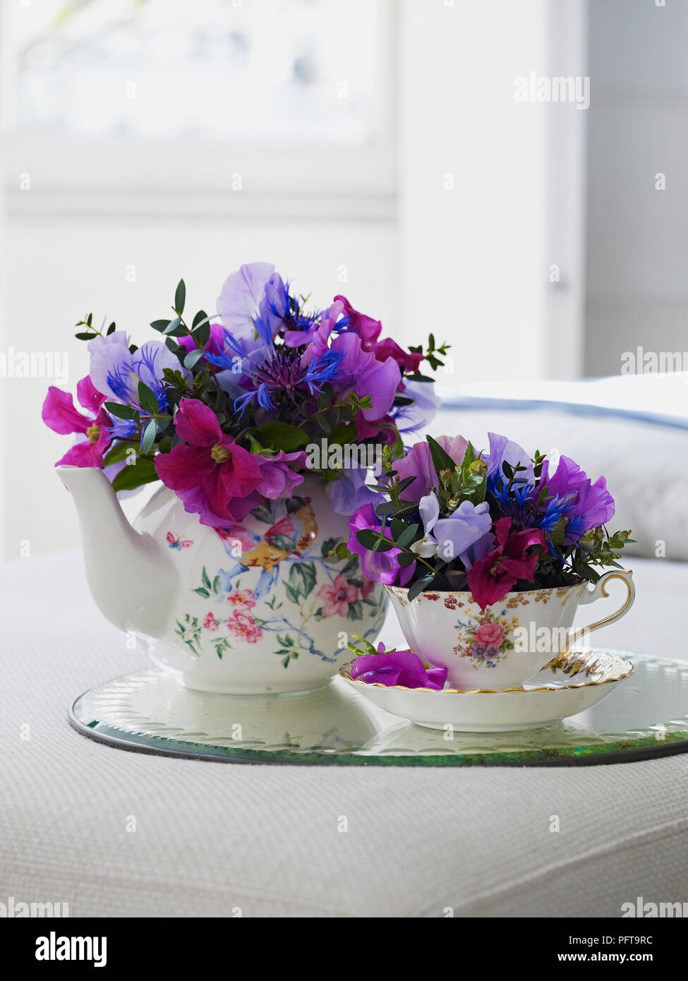 Flowers arranged in floral vintage tea set, clematis, sweet pea, centaurea, eucalyptus parvifolia Stock Photo