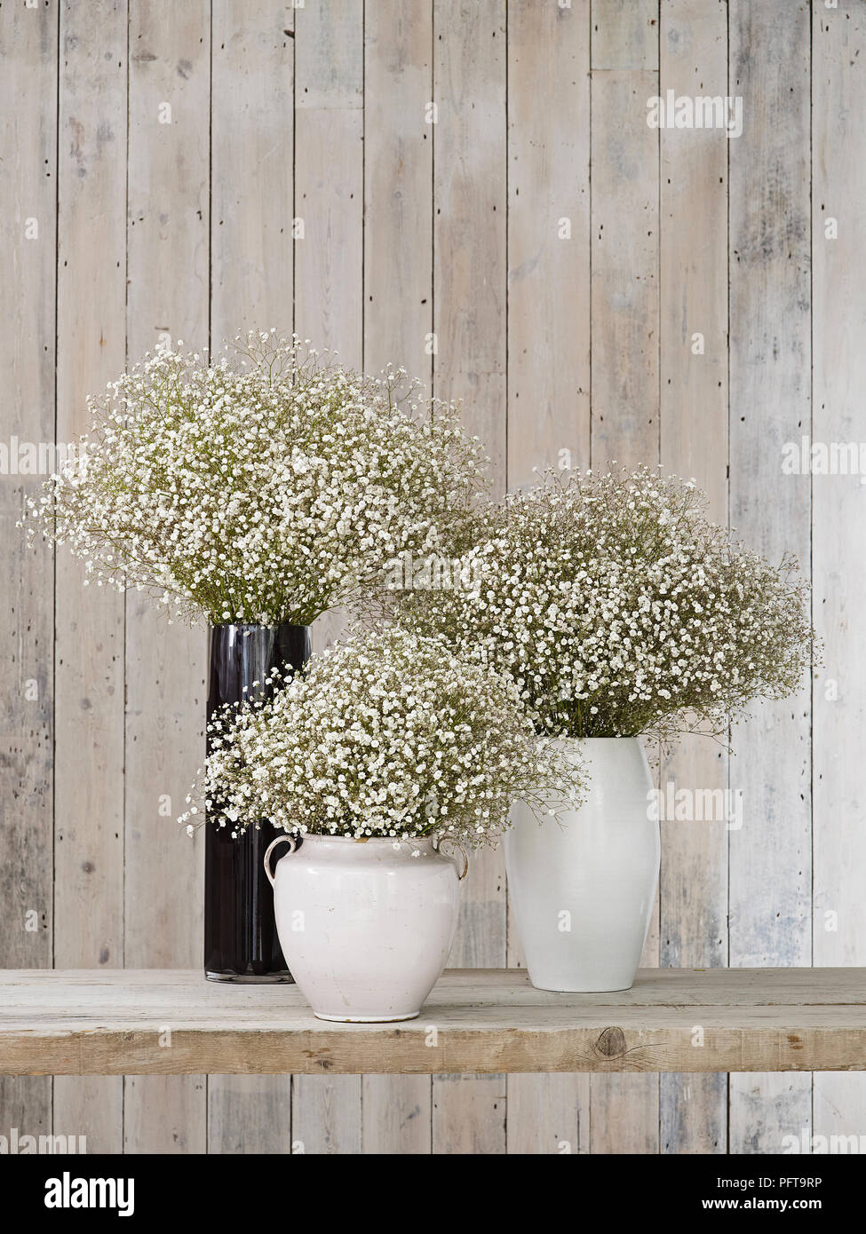 Gypsophila flowers in vases of different shapes, against wooden background Stock Photo