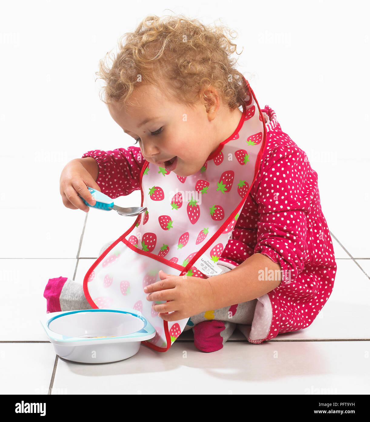 Girl (2 years) holding bowl and eating from spoon Stock Photo