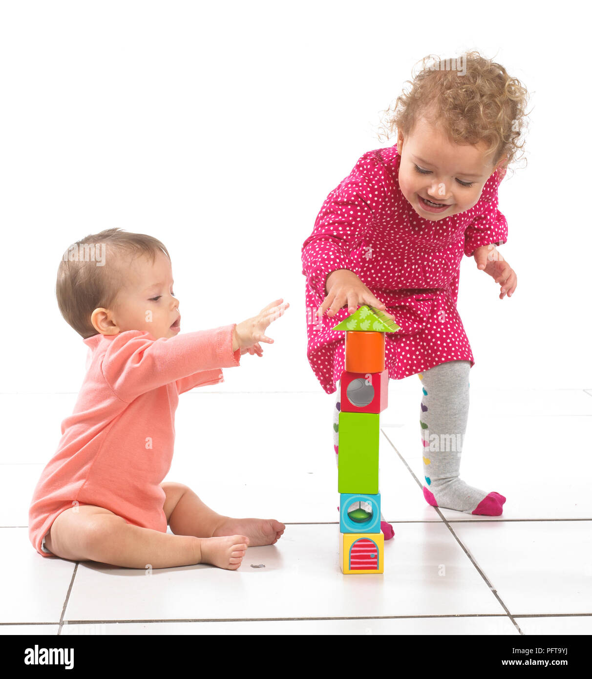 Baby girl (8 months) and toddler girl (2 years) standing building tower from blocks Stock Photo