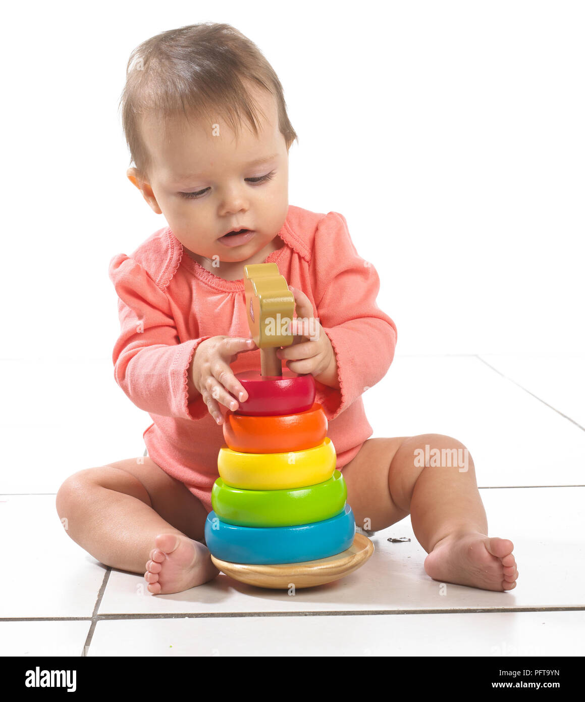 Baby girl (8 months) sitting on floor playing with stackable ring toy Stock Photo