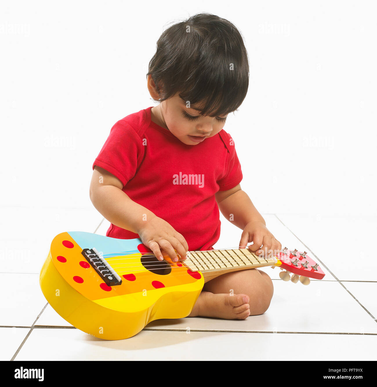 Baby boy (16 months) sitting holding colourful children's guitar Stock Photo