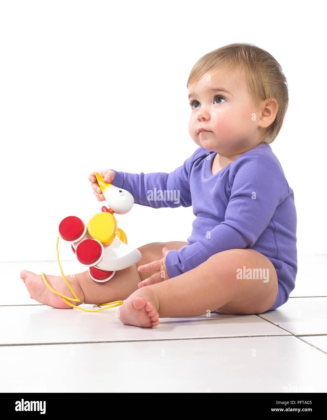 Baby girl sitting playing with pull along toy duck, 12 months Stock Photo
