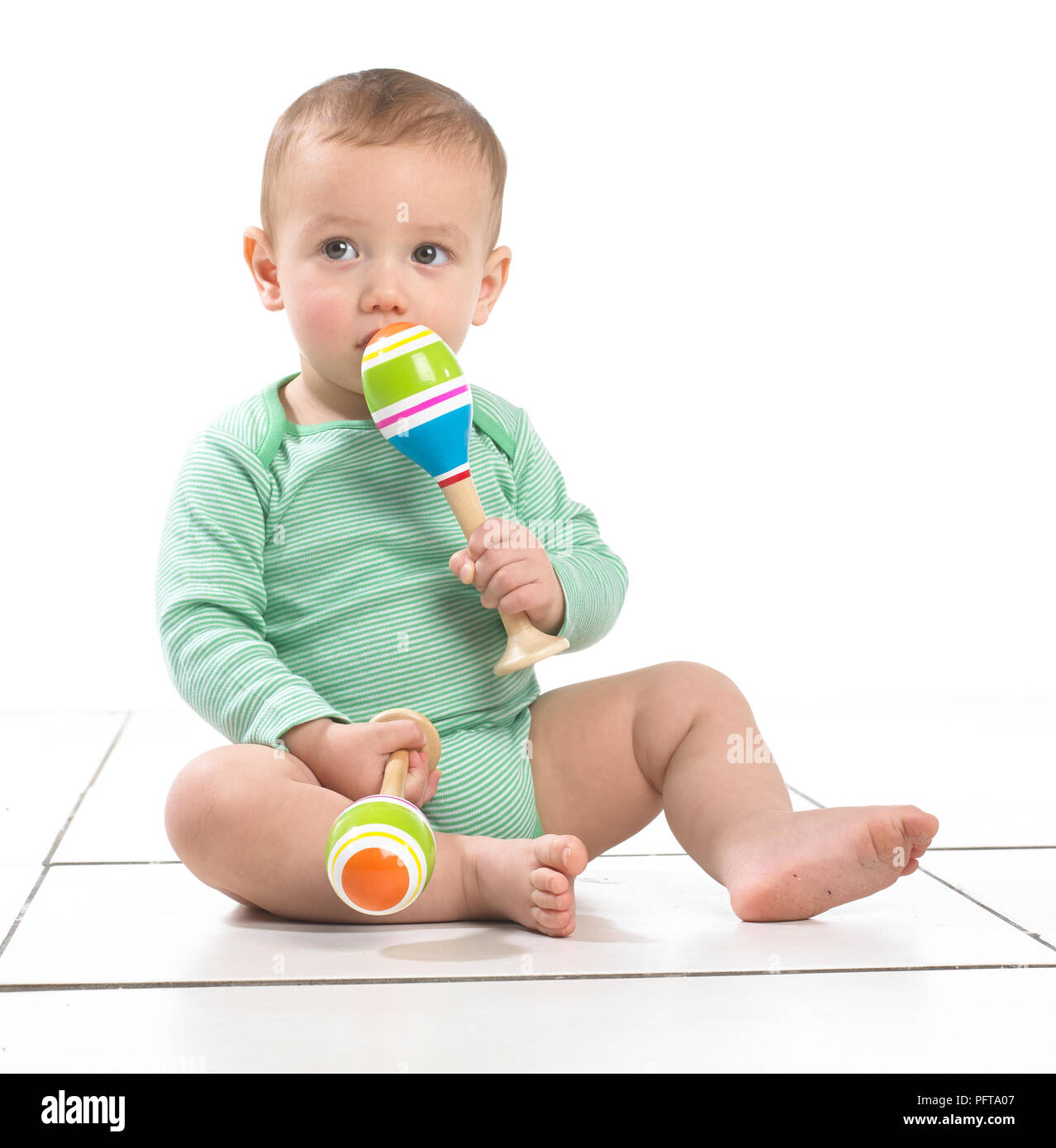 Baby boy (12.5 months) sitting playing with maracas Stock Photo