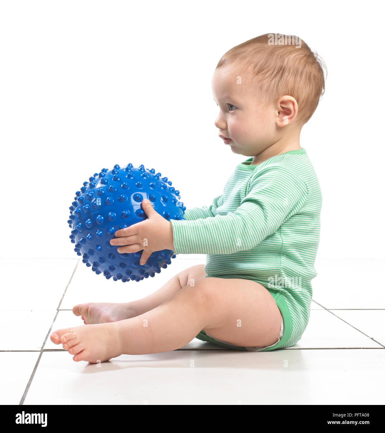 Baby boy (12.5 months) sitting holding a bumpy ball toy Stock Photo