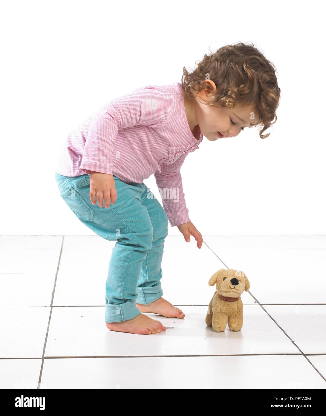 Young girl bending over towards toy dog, 2 years Stock Photo