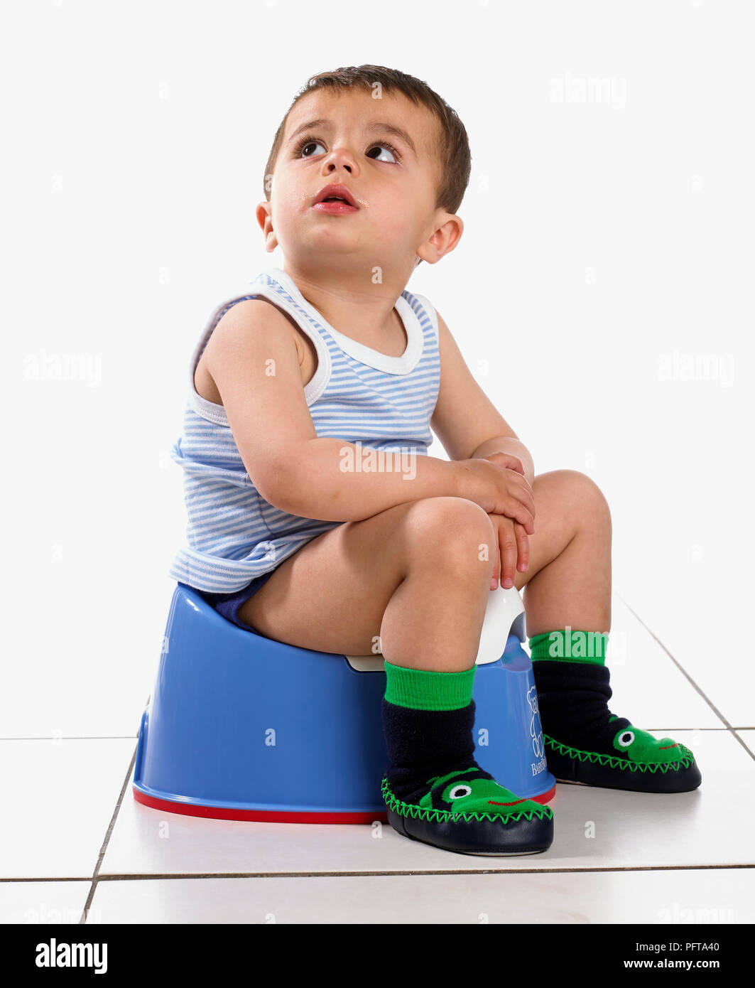 Boy wearing vest and slippers, sitting on potty, 15 months Stock Photo