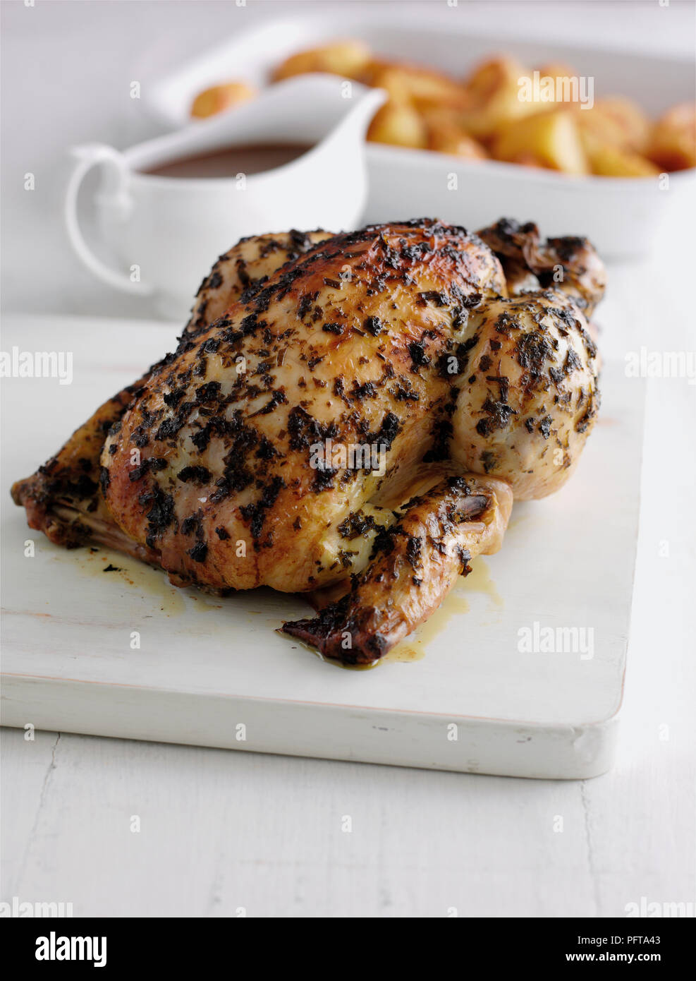 Roast chicken basted in herb butter, gravy boat and roast potatoes in background Stock Photo