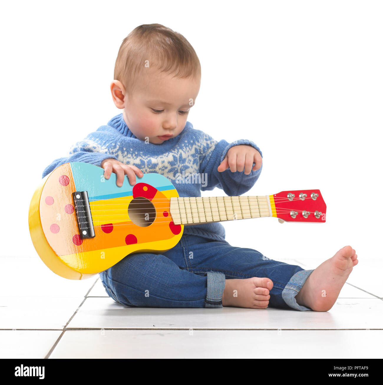 Baby boy (12.5 months) sitting playing toy guitar Stock Photo