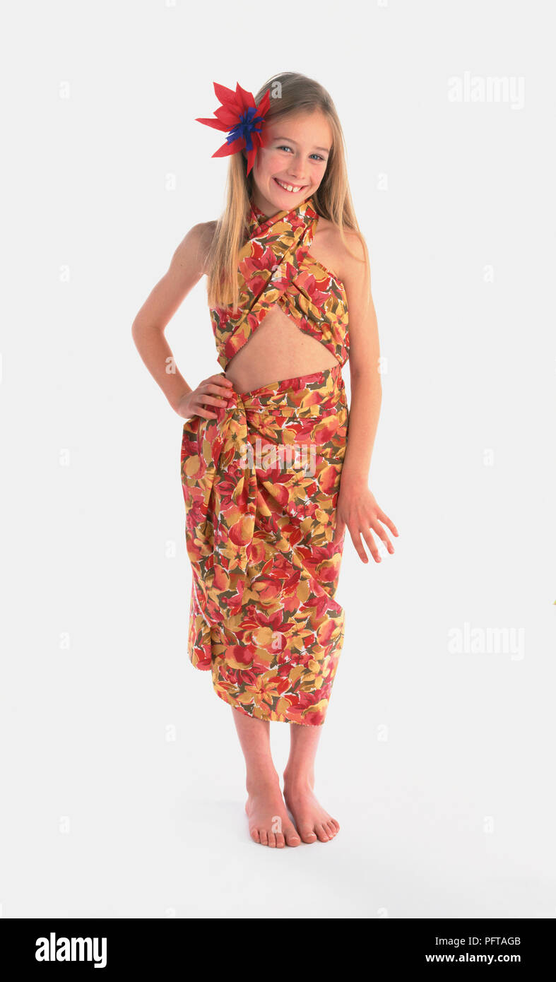 Girl wearing desert island dancer costume, bright sarong, red flower in her hair, standing with hand on hip, smiling Stock Photo