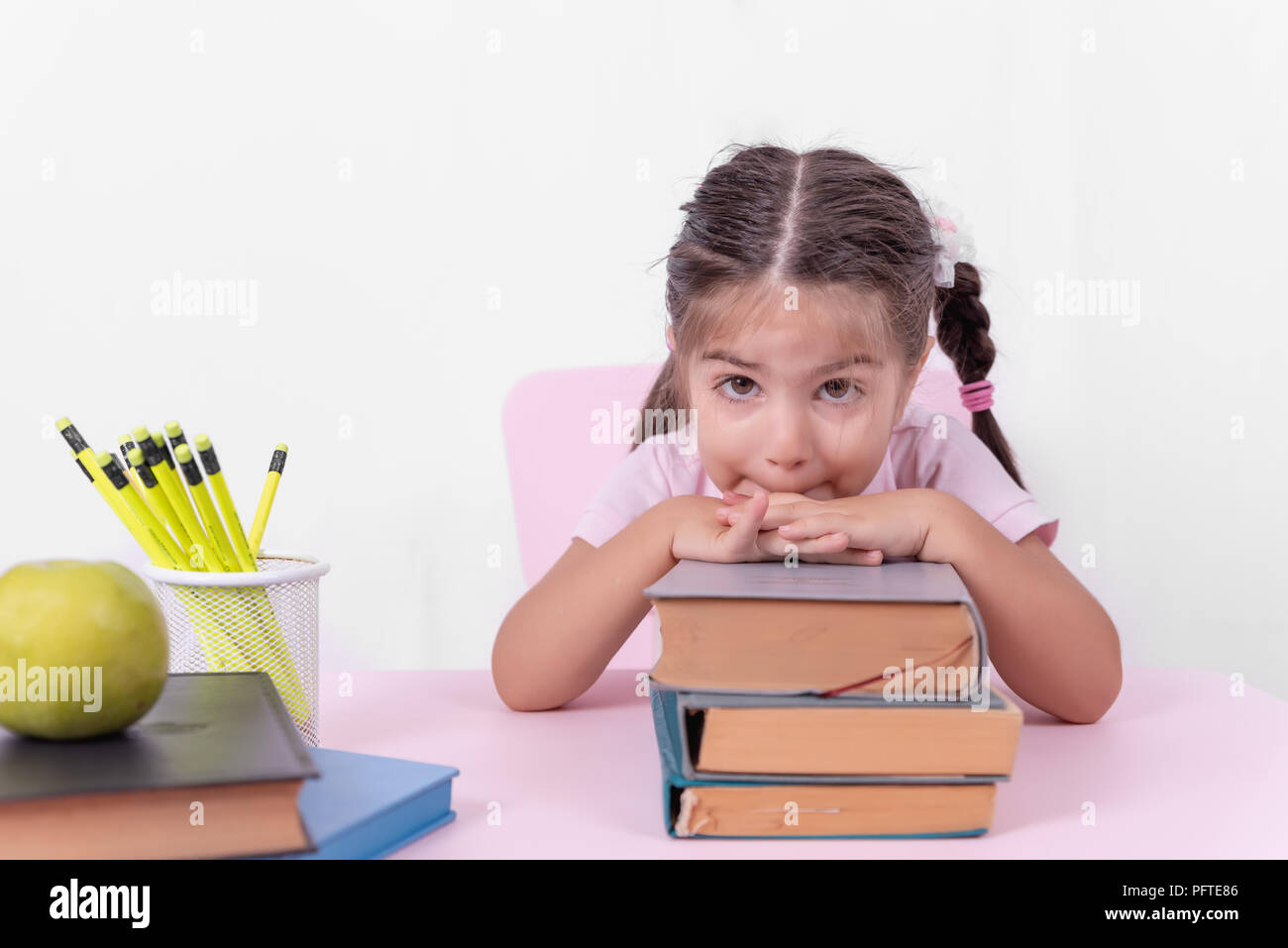 Cute little girl in school uniform looks thoughtful on books.Selective