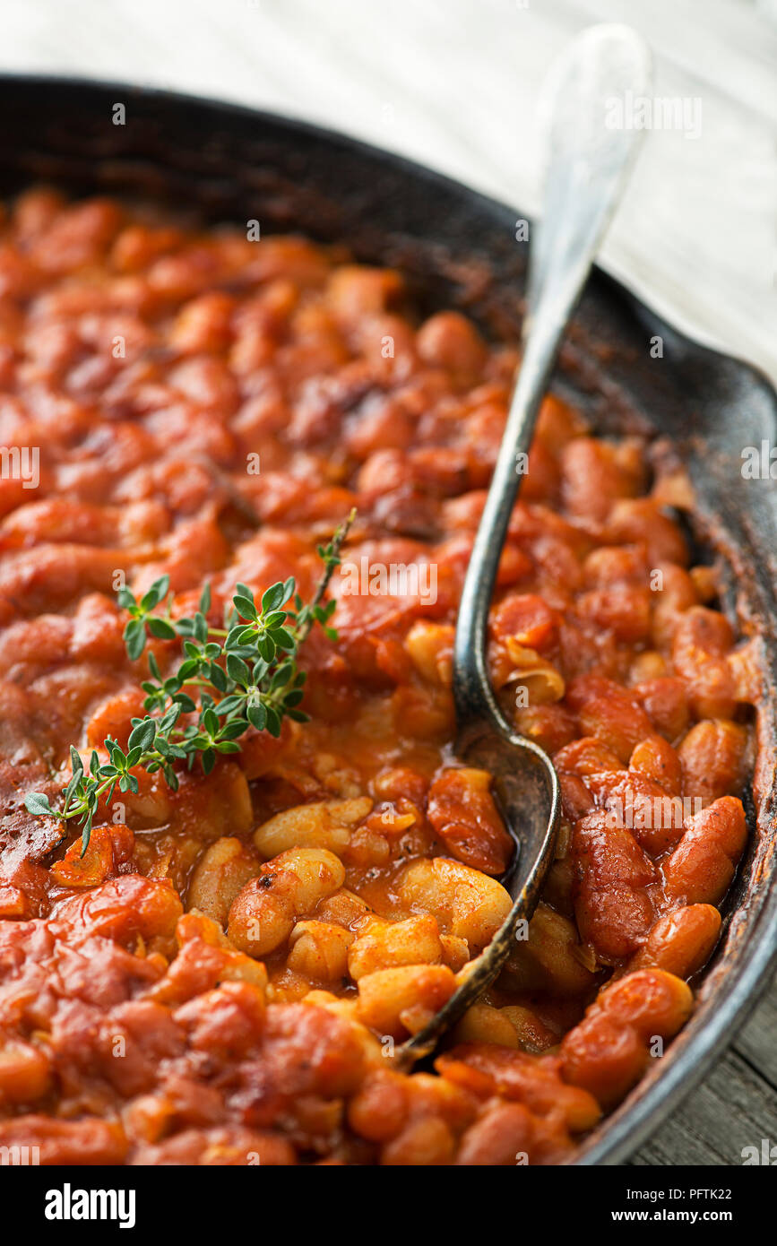 Baked beans stew with tomato sauce and meat with herbs close up Stock Photo