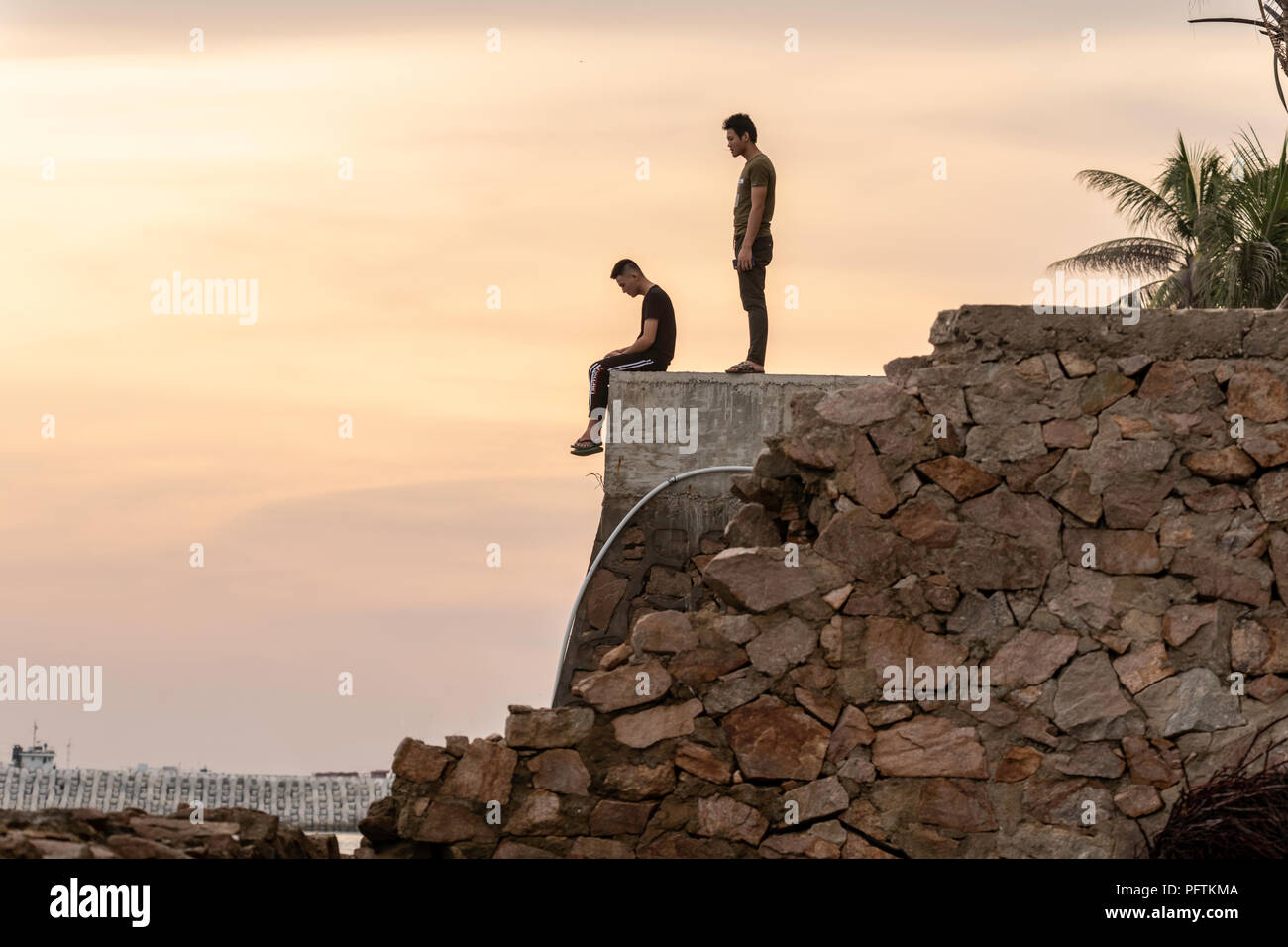 mankind, cliff edge sitting and standing man, silhouette, concept of evolution Stock Photo