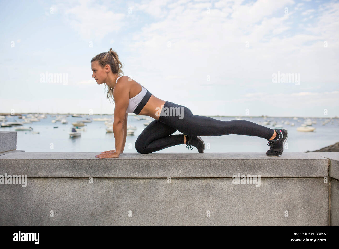 Young Adult Woman in Fitness Attire Exercising on Stone Wall Stock Photo