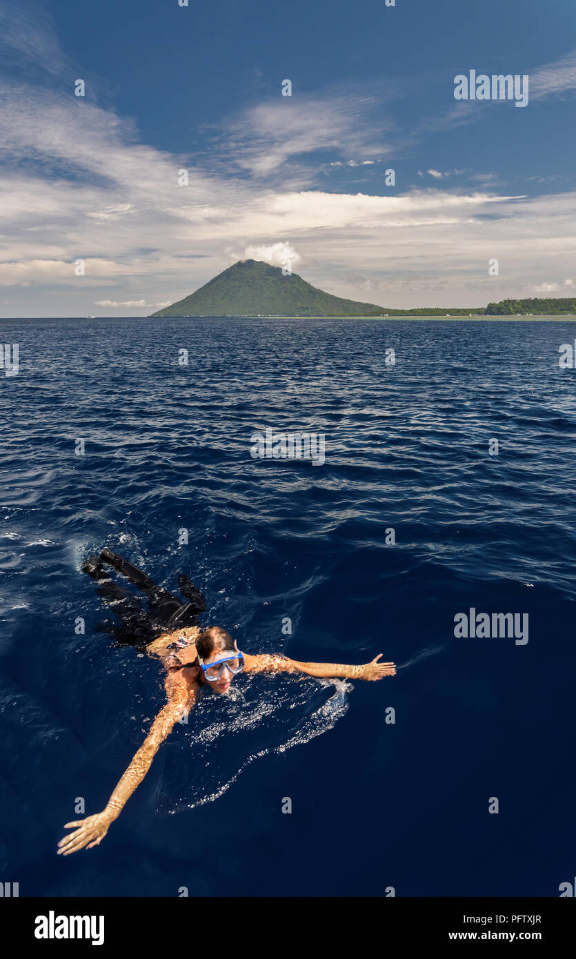 A girl swimming and snorkeling in Celebes sea by Bunaken islands with volcano in the background close to Manado, Indonesia Stock Photo