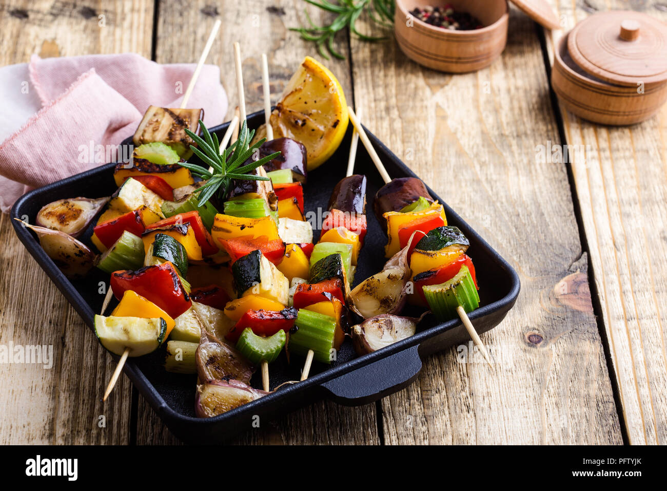 Grilled colorful vegetables skewers on cast iron skillet. Vegan summer meal on rustic wooden table Stock Photo