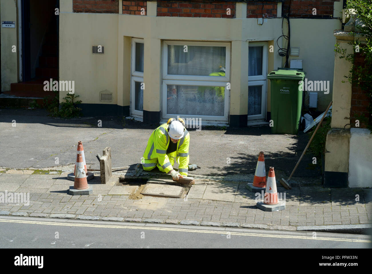 workman wearing high visibility safety clothing carrying out repairs to a drain cover on a pavement in southsea england uk Stock Photo