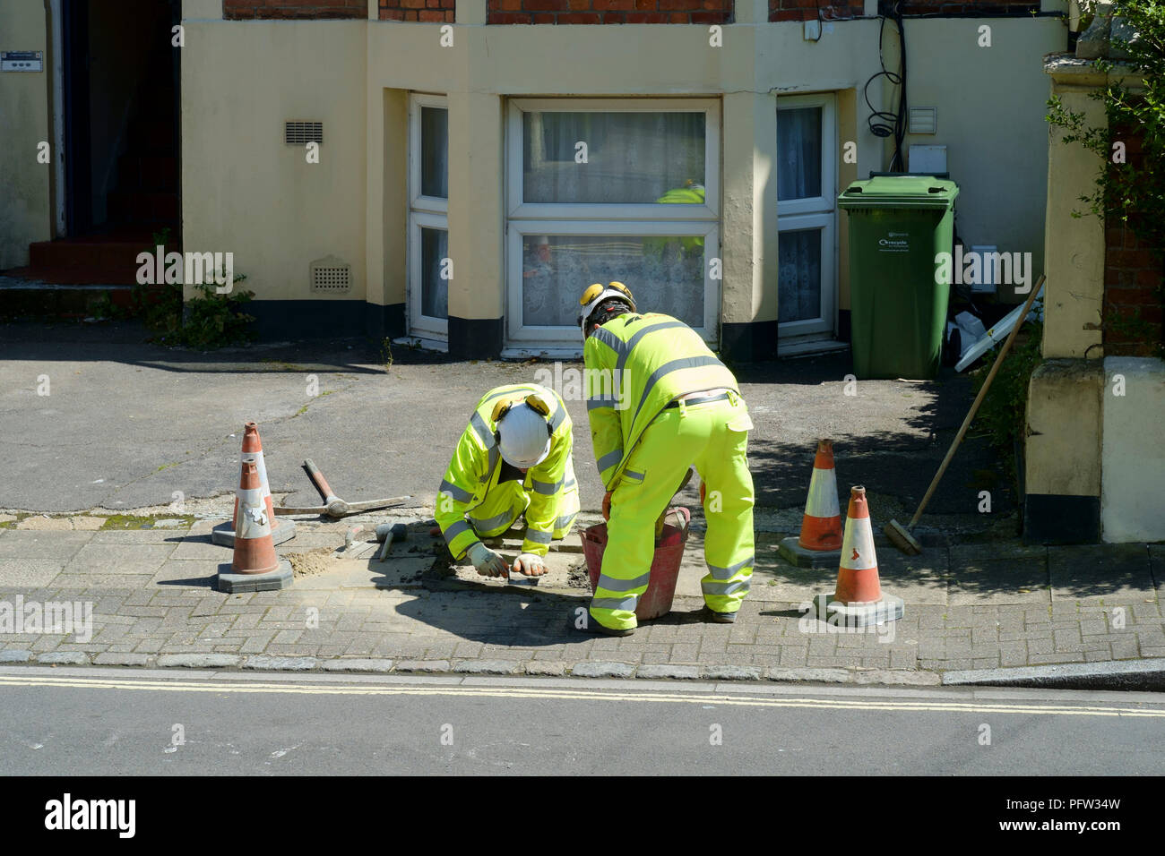 workmen wearing high visibility safety clothing carry out repairs to a drain cover on a pavement in southsea england uk Stock Photo