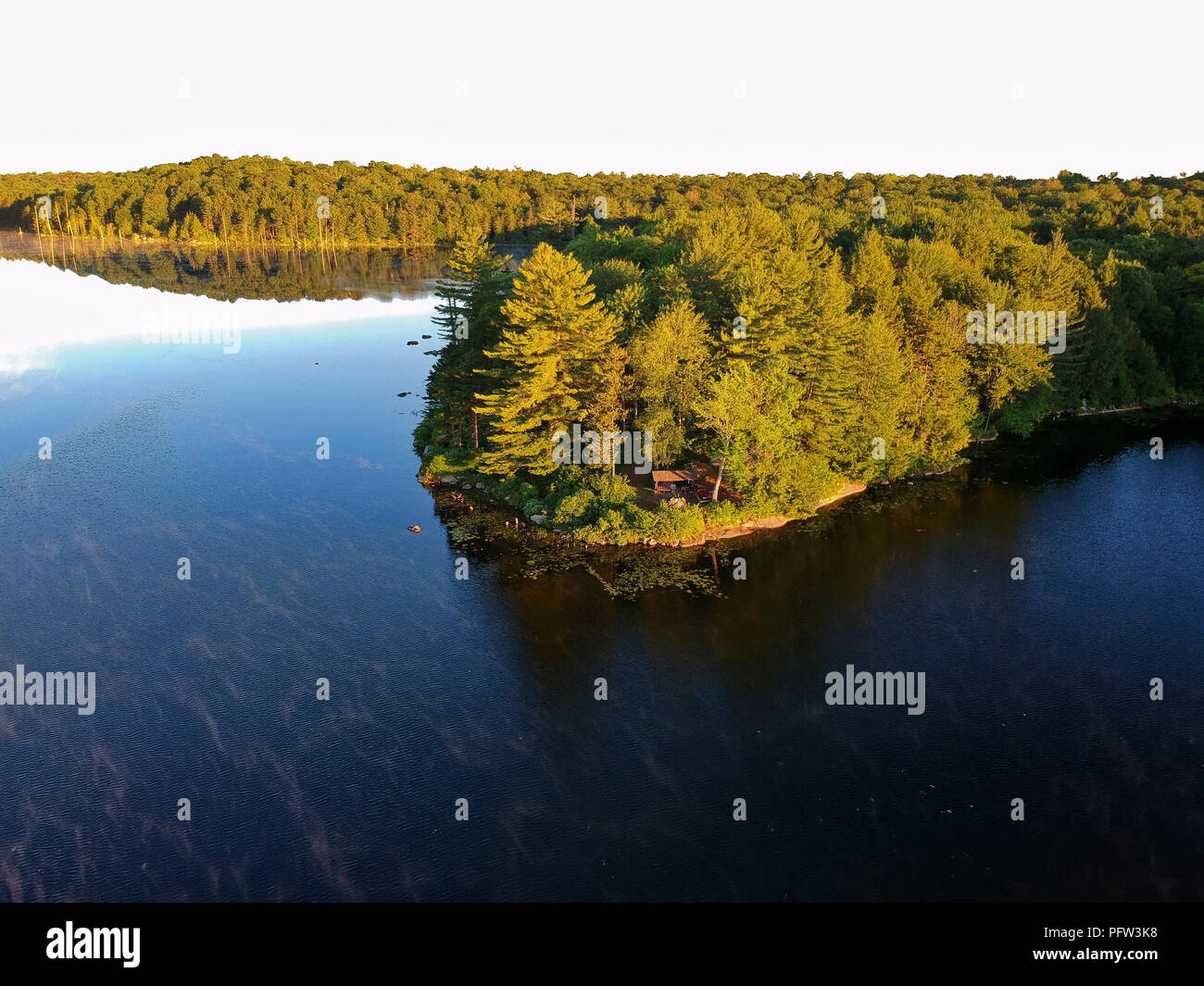 Aerial drone image of a Log cabin Lean-to shelter and campfire on a lake in the Adirondack Mountains. Bird's eye view of a waterfront campsite Stock Photo