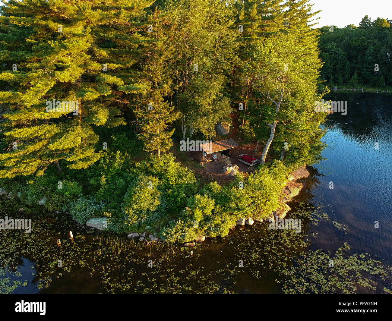 Aerial drone image of a Log cabin Lean-to shelter and campfire on a lake in the Adirondack Mountains. Bird's eye view of a waterfront campsite Stock Photo